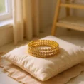 Close-up shot of a set of gold bangles with embedded stones resting on a silk embroidered cushion, soft natural light from a nearby window casting gentle shadows, the sc